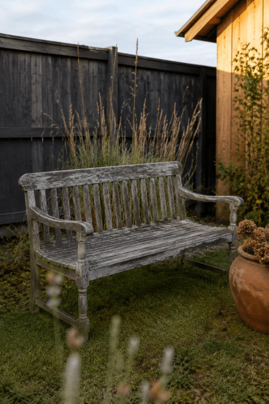 Старая посеревшая садовая скамья из сосны с облезшим лаком до реставрации на дачной лужайке